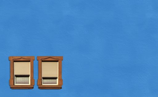 Two symmetrical vintage wooden windows with shutters isolated on the vibrant blue wall, perfect for wallpapers
