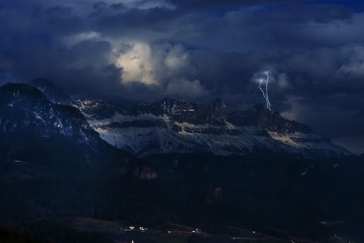 A breathtaking scene of mountains under cloudy sky getting struck by lightning at night