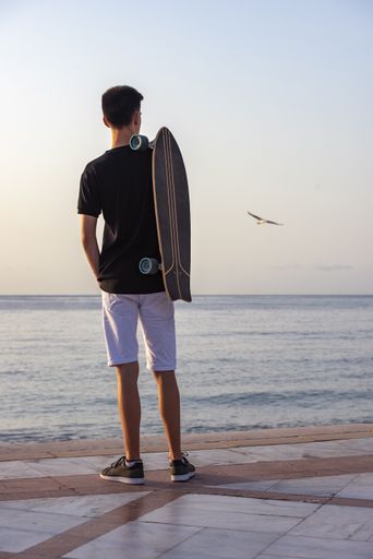A selective focus shot of a handsome young teenager with his longboard standing near an ocean