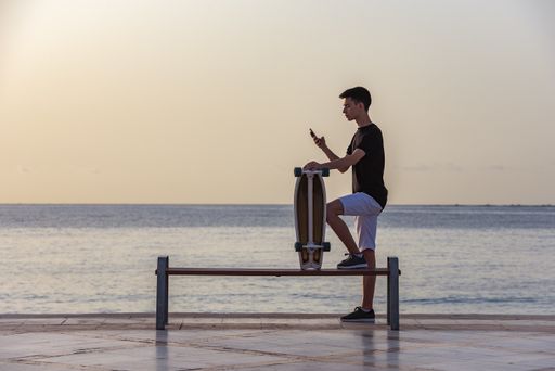 A selective focus shot of a handsome young teenager with his longboard standing near an ocean