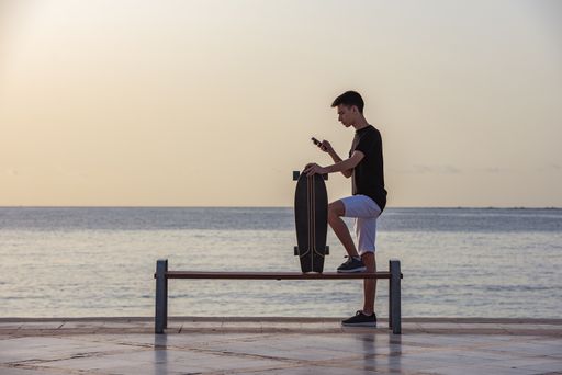 A selective focus shot of a handsome young teenager with his longboard standing near an ocean