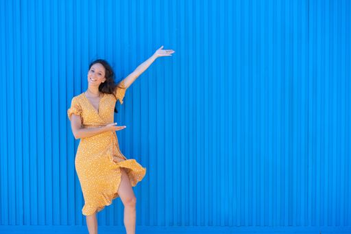 A happy woman in a light summer dress posing against a corrugated wall presenting free space for text