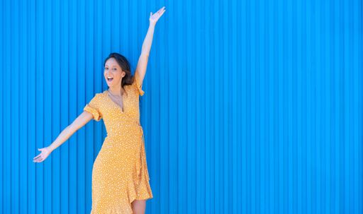 An excited woman in a light summer dress posing against a corrugated wall presenting free space for text