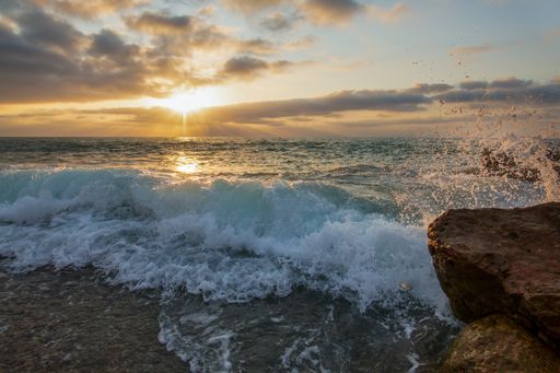 A beautiful view of the wavy ocean gleaming under the sunset piercing through the clouds