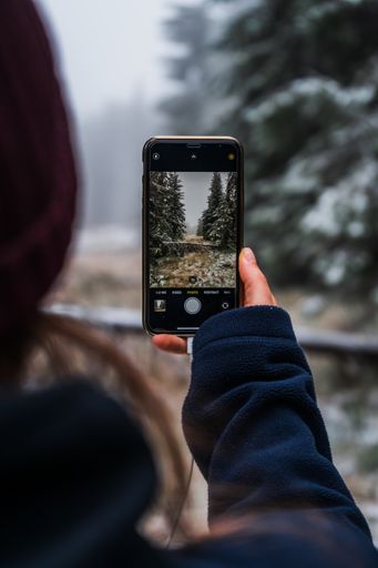 A girl taking a photo of the foggy winter forest with her phone
