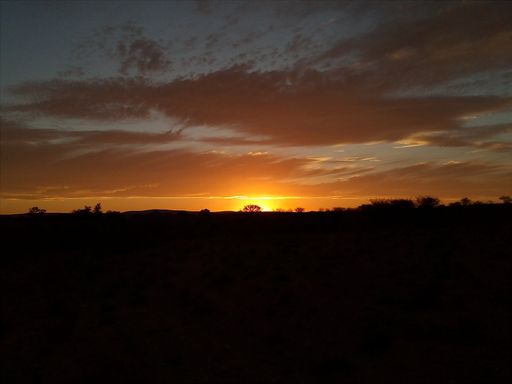 A breathtaking view of the sunset in the cloudy sky above the silhouette of a land