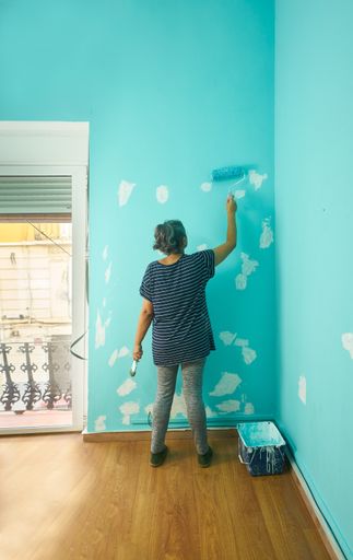A vertical shot of an adult female painting a wall cyan color under the lights