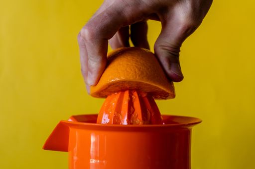 A closeup of a person squeezing orange with a squeezer isolated on a yellow background