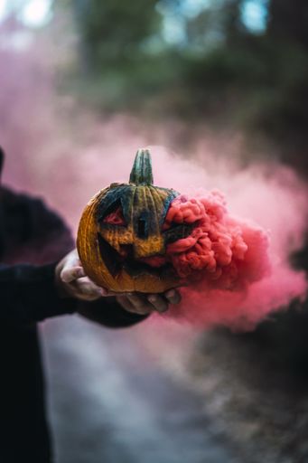 A vertical shot of a man holding a carved pumpkin with red smoke - the concept of Halloween