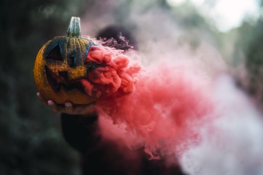 A man holding a carved pumpkin with red smoke - the concept of Halloween