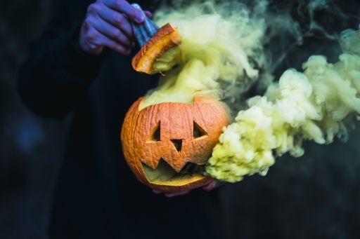 A man holding a carved pumpkin with yellow smoke coming out of it - the concept of Halloween