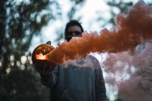 A man holding a carved pumpkin with orange smoke coming out of it - the concept of Halloween