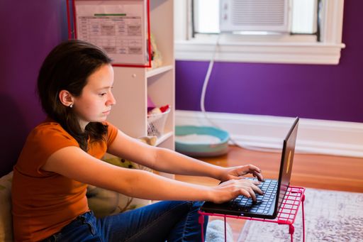 Young teenage girl using laptop. Homeschooling, hands on keyboard in bedroom.