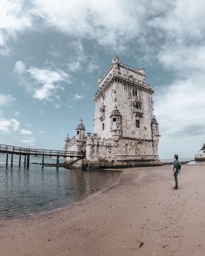 A vertical shot of a tourist standing near the Belem Tower in Lisbon, Portugal