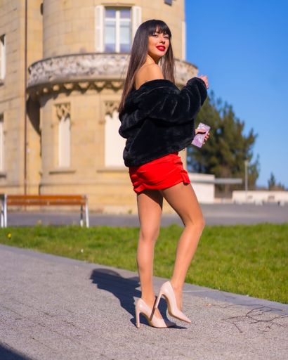 A Caucasian Brunette girl wearing red dress and posing in front of Arbide tower