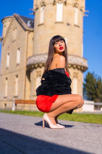 A Caucasian Brunette girl wearing red dress and posing in front of Arbide tower