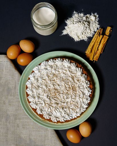 A vertical shot of a delicious cinnamon cake with the ingredients placed on a dark surface