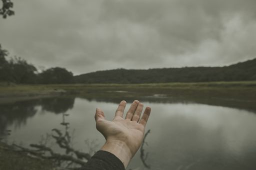 A male hand with his palm up showing the beautiful lake under the cloudy sky