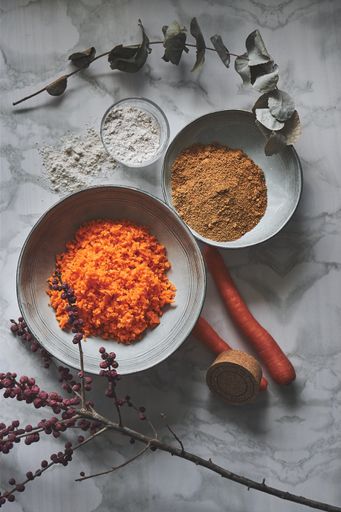A vertical shot of the ingredients for carrot cookies, such as cinnamon, flour, and shredded carrot, placed on a marble surface