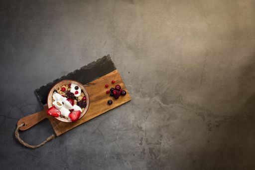 Top view of a nutritious and healthy breakfast with muesli, yogurt and seasonal red berries on a concrete background with rays of early morning light