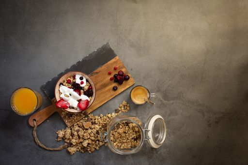 Top view of a nutritious and healthy breakfast with muesli, yogurt and seasonal red berries on a concrete background with rays of early morning light