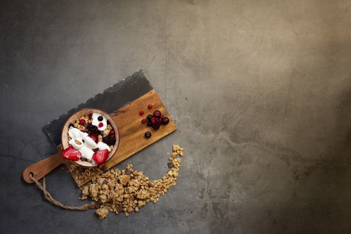Top view of a nutritious and healthy breakfast with muesli, yogurt and seasonal red berries on a concrete background with rays of early morning light