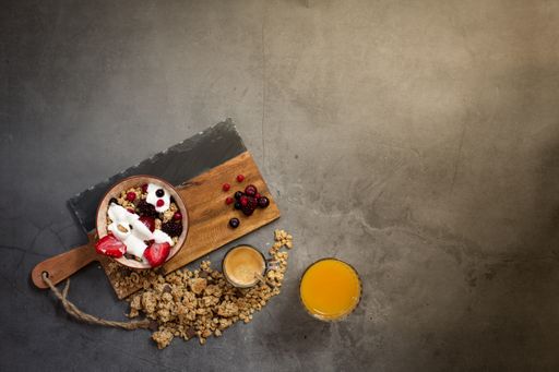 Top view of a nutritious and healthy breakfast with muesli, yogurt and seasonal red berries on a concrete background with rays of early morning light