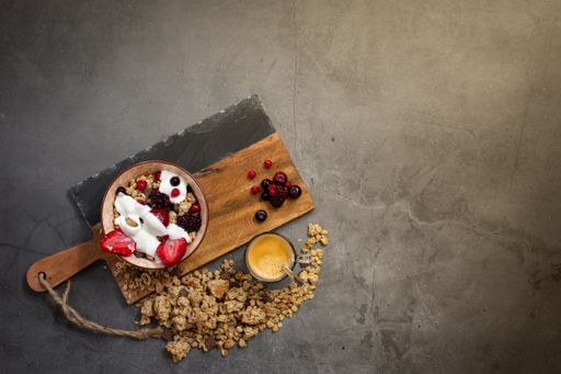Top view of a nutritious and healthy breakfast with muesli, yogurt and seasonal red berries on a concrete background with rays of early morning light