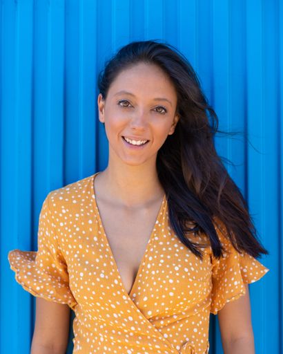 A vertical shot of an attractive young lady wearing a summer dress posing in front of a blue wall