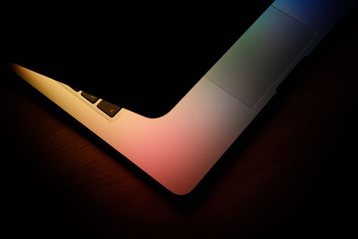 A closeup shot of the rainbow screen of a half closed laptop illuminated the keyboard