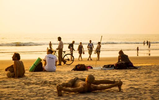 A group of People relaxing on the sandy beach at sunset, a man doing split