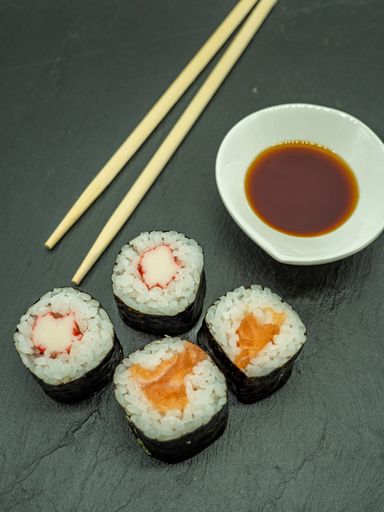 A vertical closeup shot of sushi rolls, soy sauce and a pair of wooden chopsticks
