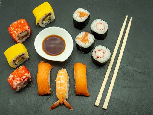 A top view of sushi rolls with shrimp and salmon served with soy sauce and chopsticks