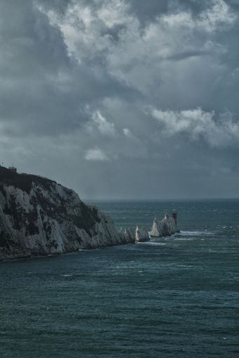 A vertical cinematic shot of rock formations in the sea under bright cloudy sky