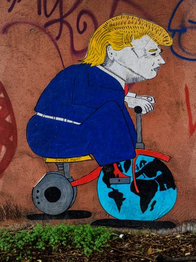 Wall art representing Donald Trump playing with the Earth like a child with his toy bike, street art by QWERTY, Rome