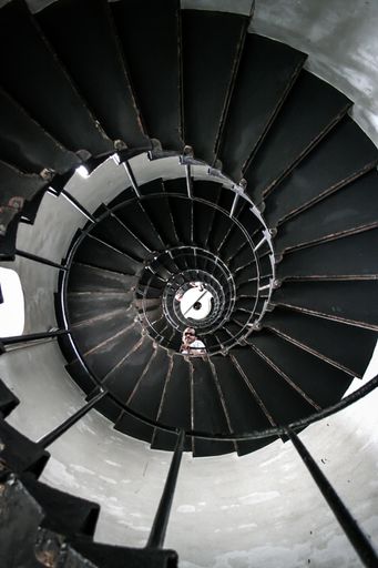 A low angle shot of a person looking down from a black spiral staircase with metallic rails
