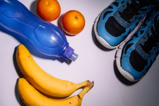 A top view of running shoes, healthy fresh fruits, and a bottle of water sports activity set on a white surface