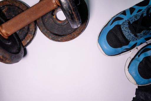 A flat lay shot of training sports shoes and a rusty iron dumbbell on a white background with a copy space