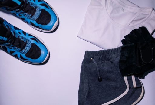 A top view of training shoes with a female sports outfit and workout gloves on a white surface