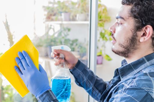 A young Caucasian man cleaning window glass with sprayer and cloth