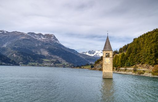 The Submerged Clock Tower in the Reschensee surrounded by hills in South Tyrol, Italy