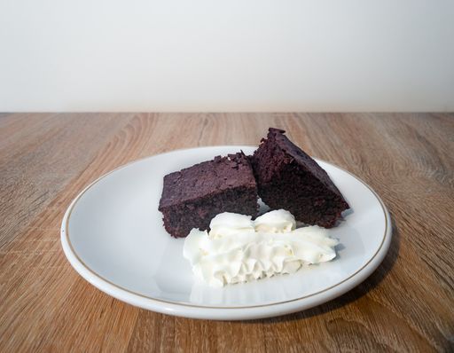 A vertical shot of a brownie cake with ice cream on a white plate on a wooden surface