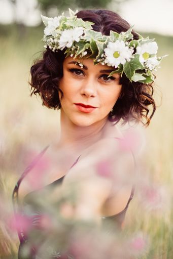 A shallow focus of an adult female with a flower wreath on her head posing in a field