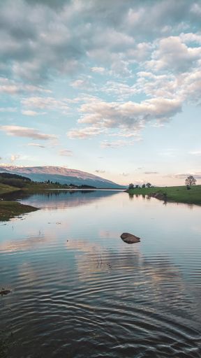 The vertical shot of a river surrounded by grass coasts and slopes