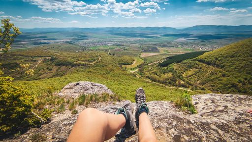 A person sits on a large rock with a scenic mountain backdrop