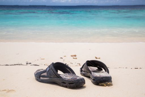 The black flip-flops on the sandy beach by the wavy ocean
