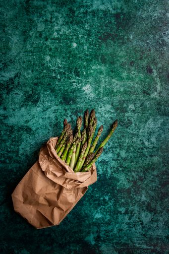 A vertical shot of organic asparaguses in a brown paper bag