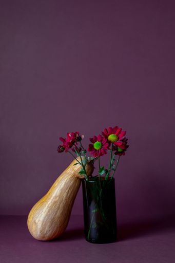 A vertical shot of a pumpkin and a vase of flowers against a purple background