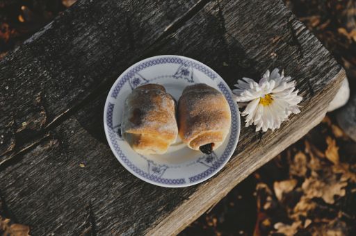 A top view of a pastry stuffed with jam served on a plate on a wooden bench near a flower