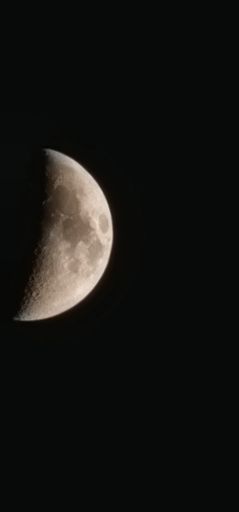 A vertical shot of the half-moon isolated on the empty dark black background for wallpapers